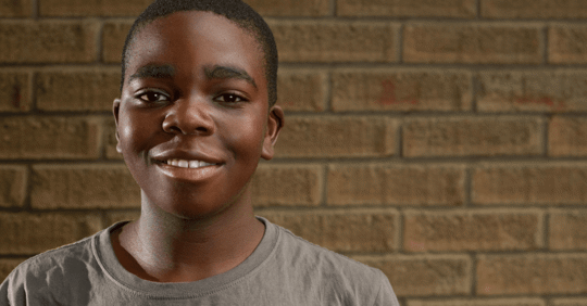 young african american teenager smiling at camera in front of a brick wall